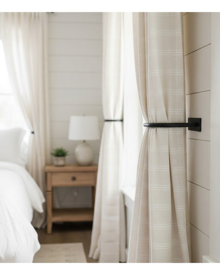 Black metal horse head curtain tie backs holding cream linen curtains in bright white bedroom with wooden nightstand - Ind...