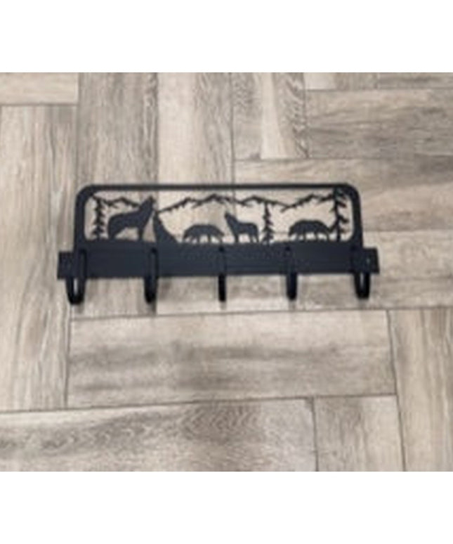 Black metal wolf silhouette coat rack with mountain forest scene design and 5 hooks mounted on light wood parquet floor
