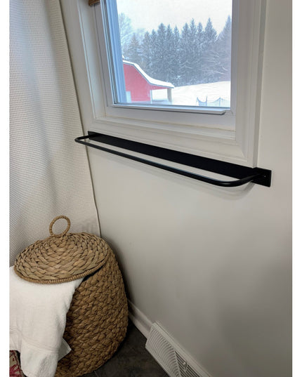 Black metal Oswego Modern Bathroom Towel Bar by Industrial Farm Co mounted below white window in minimalist room with snow...